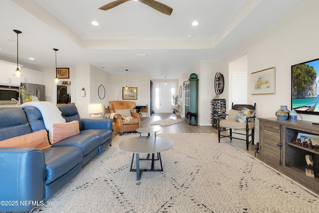 living room featuring light hardwood / wood-style floors, a raised ceiling, and ceiling fan