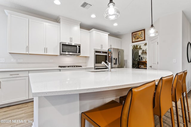 kitchen featuring a breakfast bar, white cabinetry, hanging light fixtures, stainless steel appliances, and an island with sink