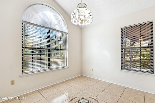 spare room with light tile patterned flooring, an inviting chandelier, and a textured ceiling