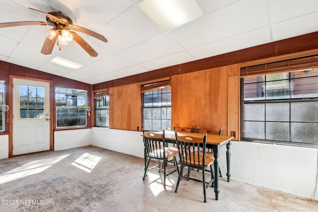 dining area with a drop ceiling, ceiling fan, and wood walls