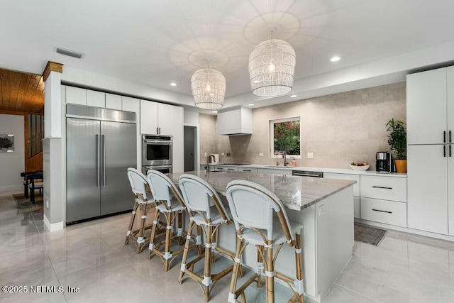 kitchen featuring sink, white cabinetry, appliances with stainless steel finishes, pendant lighting, and a kitchen island with sink