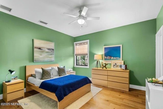 bedroom with light wood finished floors, a ceiling fan, visible vents, and baseboards