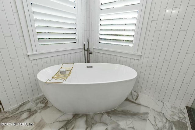 full bath featuring marble finish floor, tile walls, and a soaking tub