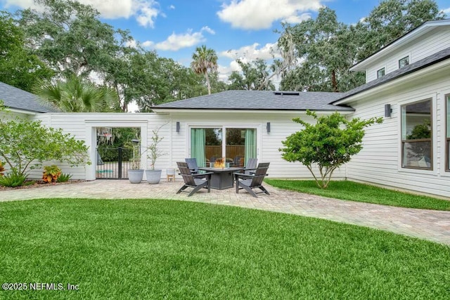 rear view of house featuring a yard, an outdoor fire pit, roof with shingles, and a patio