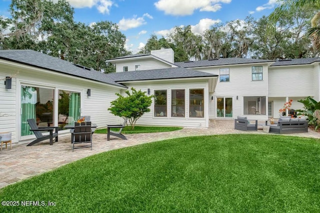 rear view of house with a lawn, a patio, a chimney, roof with shingles, and an outdoor living space