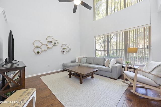 living room with dark wood-type flooring, a towering ceiling, and ceiling fan