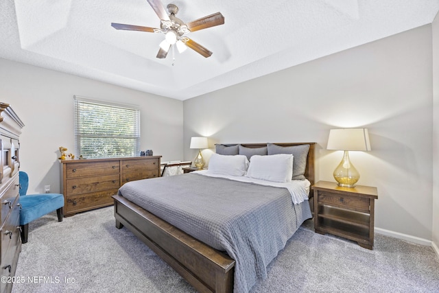 bedroom with a raised ceiling, ceiling fan, light carpet, and a textured ceiling