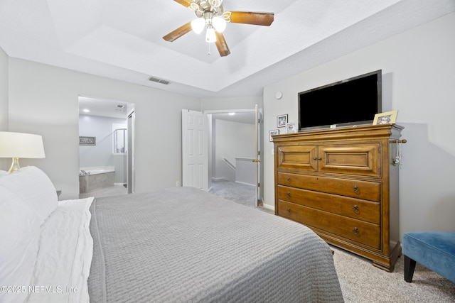 bedroom featuring ceiling fan, light colored carpet, a tray ceiling, and ensuite bath