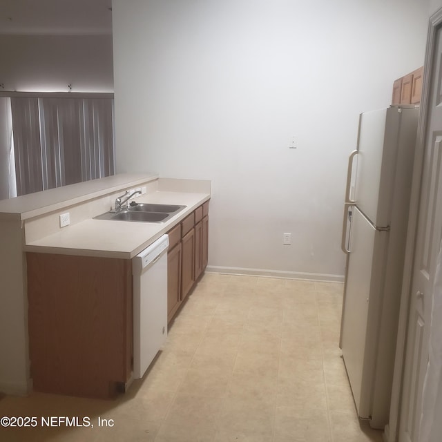 kitchen with white appliances, brown cabinets, a peninsula, light countertops, and a sink