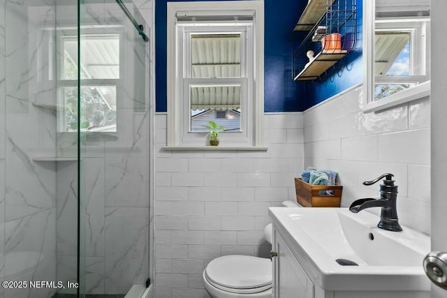 bathroom with vanity, toilet, a shower with shower door, and tile walls