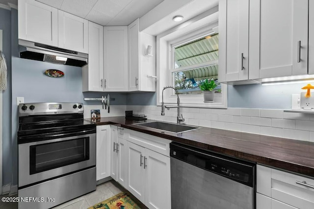 kitchen featuring sink, butcher block countertops, white cabinetry, light tile patterned floors, and appliances with stainless steel finishes