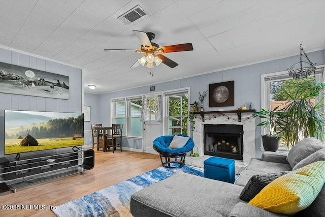 living room featuring wood-type flooring, ornamental molding, ceiling fan, and a fireplace