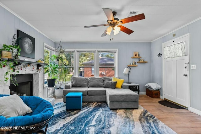 living room with hardwood / wood-style flooring, ornamental molding, ceiling fan, and a fireplace