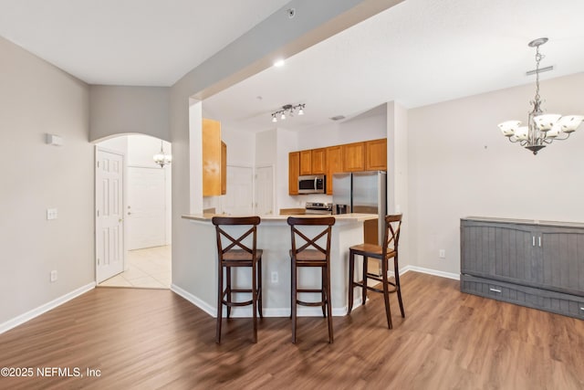 kitchen featuring an inviting chandelier, stainless steel appliances, kitchen peninsula, and a kitchen bar