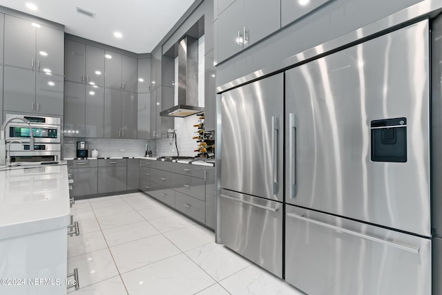 kitchen featuring gray cabinets, appliances with stainless steel finishes, backsplash, and wall chimney exhaust hood