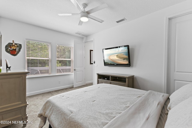 bedroom with ceiling fan, light colored carpet, and a textured ceiling