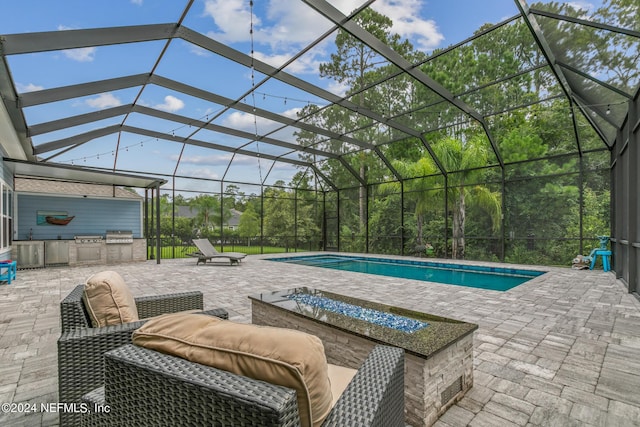 view of pool with a lanai, an outdoor kitchen, a patio area, and a fire pit