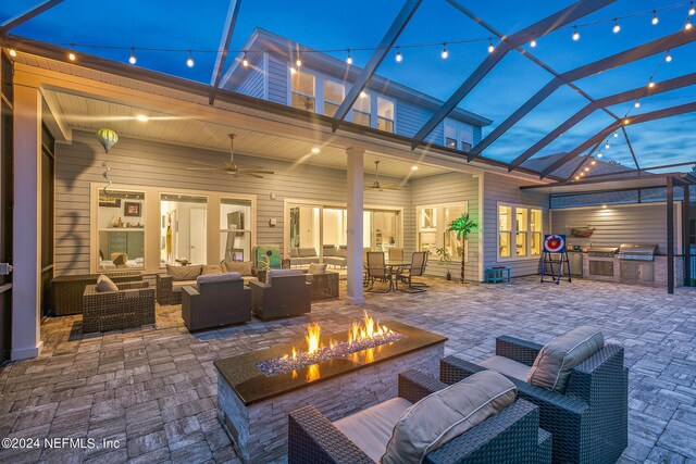 view of patio with an outdoor kitchen, an outdoor living space with a fire pit, grilling area, ceiling fan, and glass enclosure