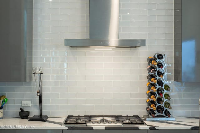 room details featuring tasteful backsplash, light stone countertops, stainless steel gas cooktop, and wall chimney exhaust hood