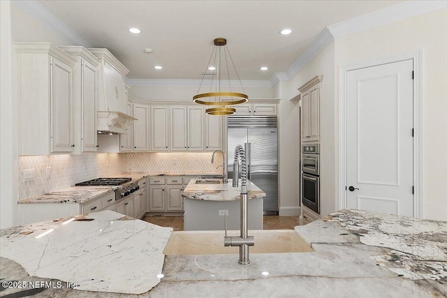 kitchen featuring appliances with stainless steel finishes, decorative light fixtures, a kitchen island with sink, crown molding, and light stone countertops