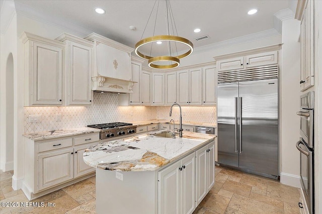 kitchen with decorative light fixtures, a kitchen island with sink, stainless steel appliances, crown molding, and light stone countertops