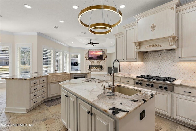 kitchen with stainless steel gas cooktop, sink, pendant lighting, light stone countertops, and a kitchen island with sink