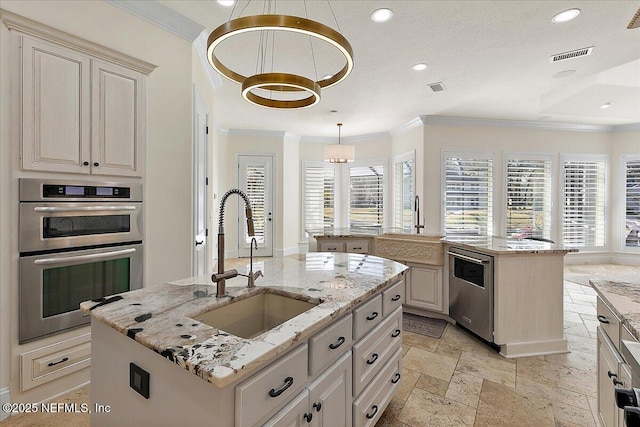 kitchen with sink, light stone counters, decorative light fixtures, a center island with sink, and appliances with stainless steel finishes