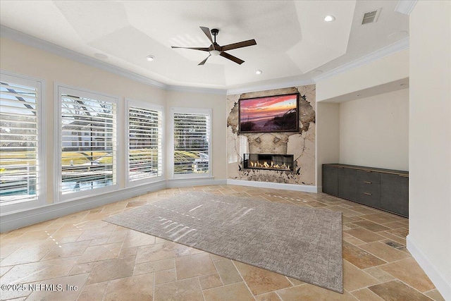 unfurnished living room featuring a raised ceiling, ornamental molding, a large fireplace, and ceiling fan