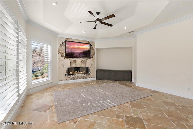 unfurnished living room with a tray ceiling, a high end fireplace, ornamental molding, and ceiling fan