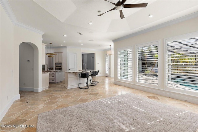 kitchen featuring a kitchen bar, light stone counters, decorative light fixtures, ornamental molding, and an island with sink