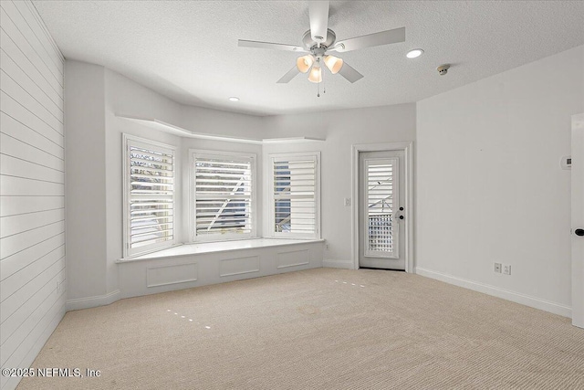 carpeted spare room with ceiling fan, wooden walls, and a textured ceiling