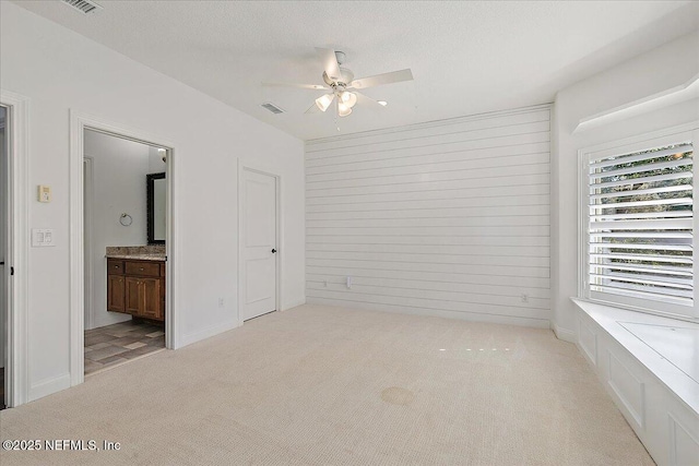 unfurnished bedroom with ceiling fan, light colored carpet, connected bathroom, and a textured ceiling