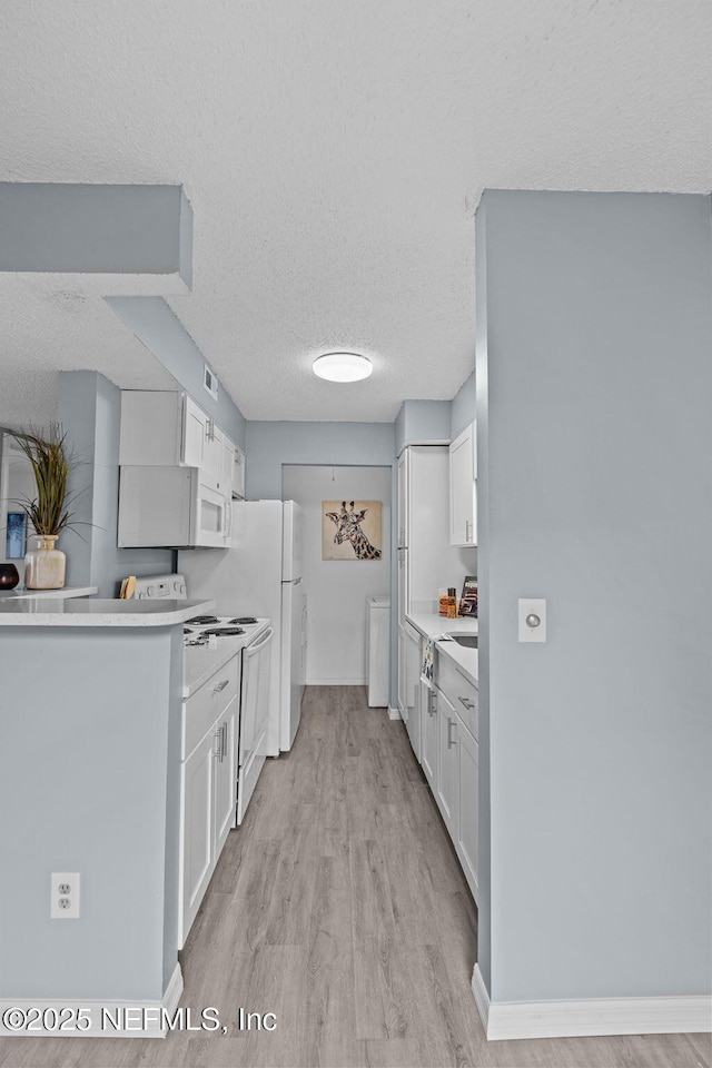 kitchen featuring white cabinetry, light wood-type flooring, a textured ceiling, and white appliances