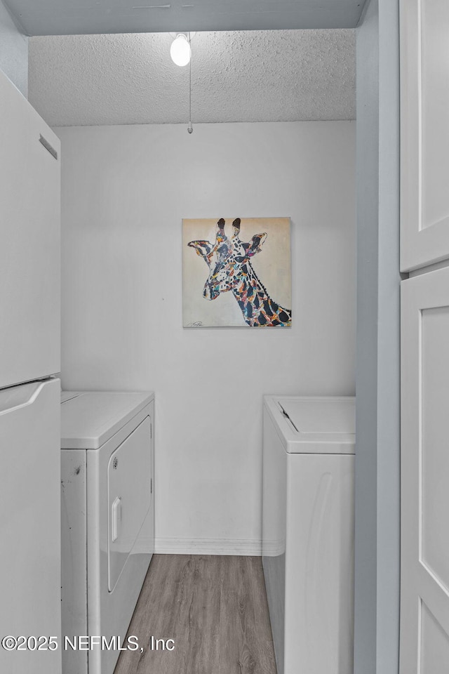 laundry room with washing machine and dryer, a textured ceiling, and light hardwood / wood-style flooring