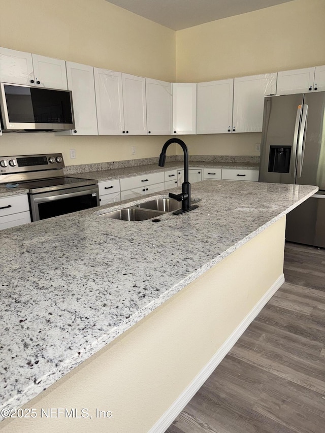 kitchen with stainless steel appliances, white cabinetry, light stone countertops, and sink