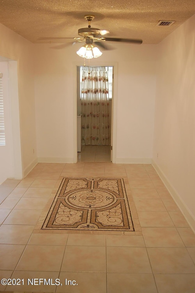 tiled empty room featuring ceiling fan and a textured ceiling