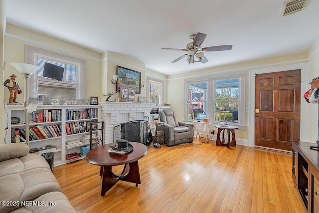 living room featuring ceiling fan, a brick fireplace, and light hardwood / wood-style flooring