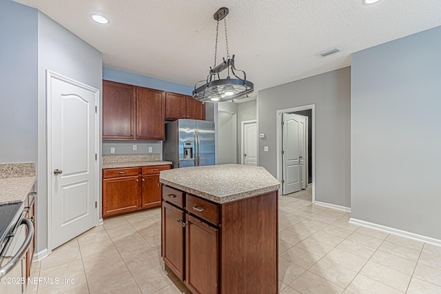 kitchen with appliances with stainless steel finishes, hanging light fixtures, a textured ceiling, a kitchen island, and light tile patterned flooring