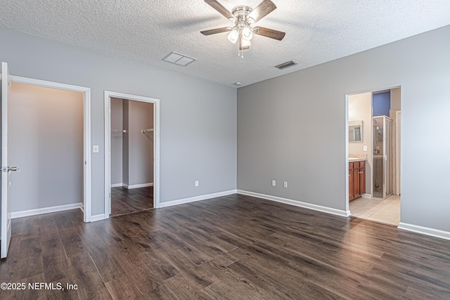 unfurnished bedroom featuring a spacious closet, a textured ceiling, and dark hardwood / wood-style flooring