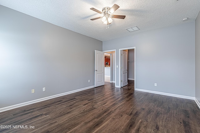 unfurnished bedroom with dark wood-type flooring, ceiling fan, a textured ceiling, a walk in closet, and a closet