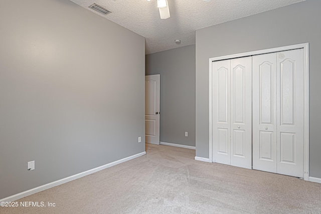 unfurnished bedroom with ceiling fan, light colored carpet, a closet, and a textured ceiling