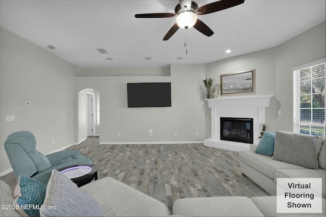 living room with arched walkways, a glass covered fireplace, baseboards, and wood finished floors