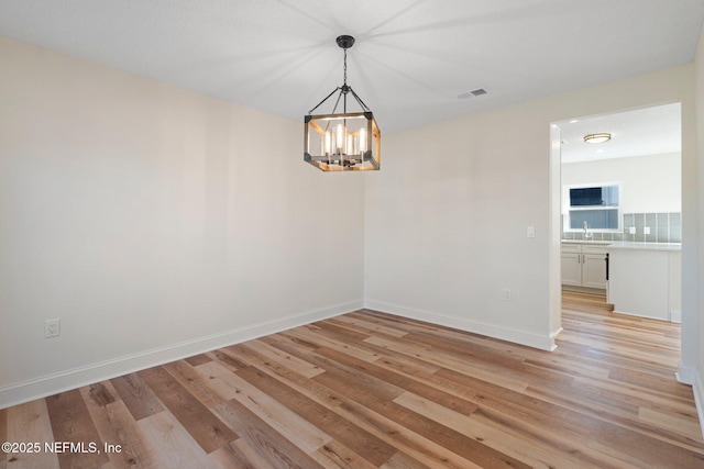 unfurnished room with sink, light hardwood / wood-style flooring, and a chandelier