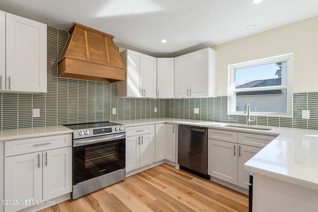 kitchen with sink, custom range hood, white cabinets, and appliances with stainless steel finishes