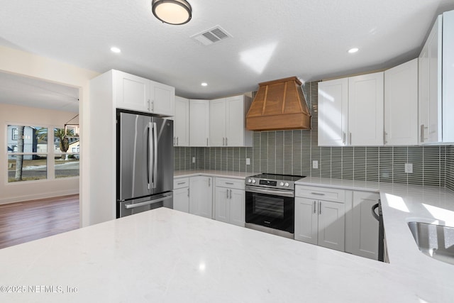 kitchen with custom exhaust hood, white cabinetry, appliances with stainless steel finishes, and backsplash