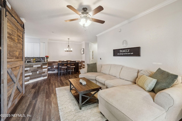 living room with hardwood / wood-style floors, ceiling fan with notable chandelier, ornamental molding, and a barn door