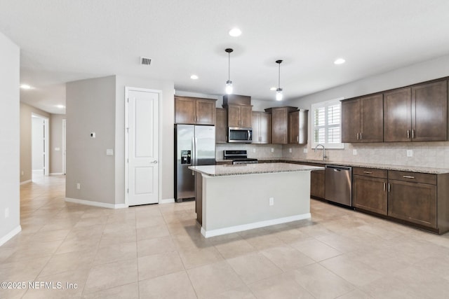 kitchen featuring hanging light fixtures, stainless steel appliances, light stone counters, a kitchen island, and decorative backsplash