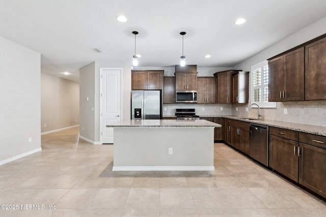 kitchen with pendant lighting, sink, stainless steel appliances, a center island, and light stone counters