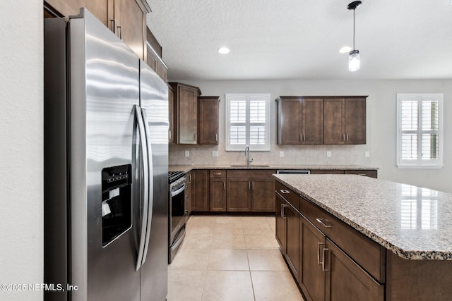 kitchen featuring light stone countertops, appliances with stainless steel finishes, light tile patterned floors, and dark brown cabinetry