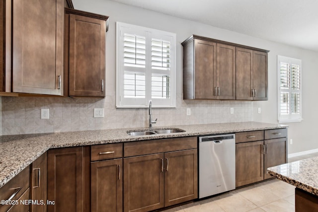 kitchen featuring sink, dishwasher, plenty of natural light, light stone countertops, and light tile patterned flooring